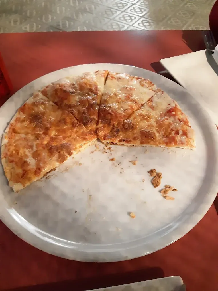 Una pizza de queso parcialmente comida reposa sobre un plato blanco redondo sobre una mesa roja.