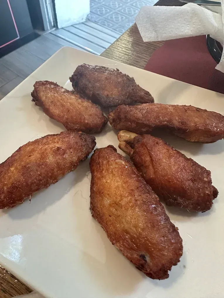 Un plato blanco contiene siete alitas de pollo fritas y doradas. Algunas tienen el condimento visible.