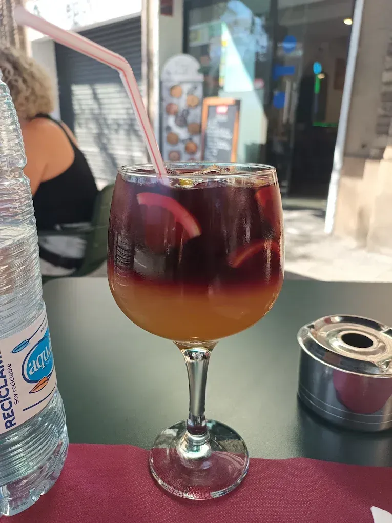 Cóctel de sangría en un vaso alto con pajita en una mesa al aire libre.