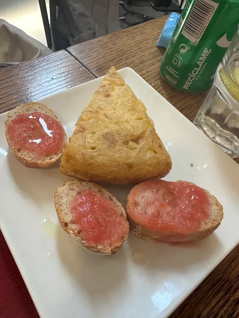 Un plato con tortilla española y tres rebanadas de pan con tomate y aceite. Al fondo, una lata verde.