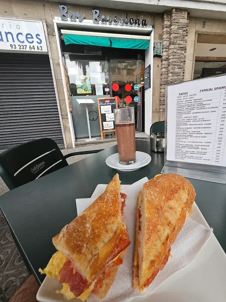 Un sándwich y una bebida están en una mesa frente a una cafetería. El sándwich está cortado por la mitad, revelando su contenido.