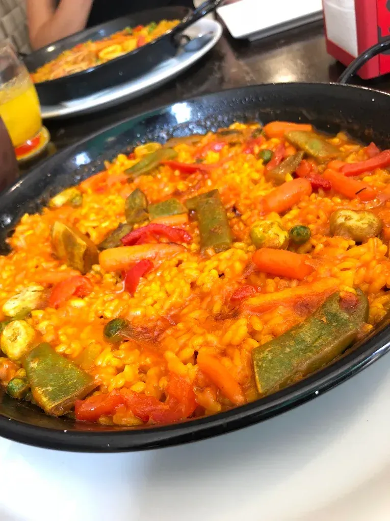 Plato de paella relleno de arroz amarillo y verduras, incluidas zanahorias, pimientos rojos y judías verdes.