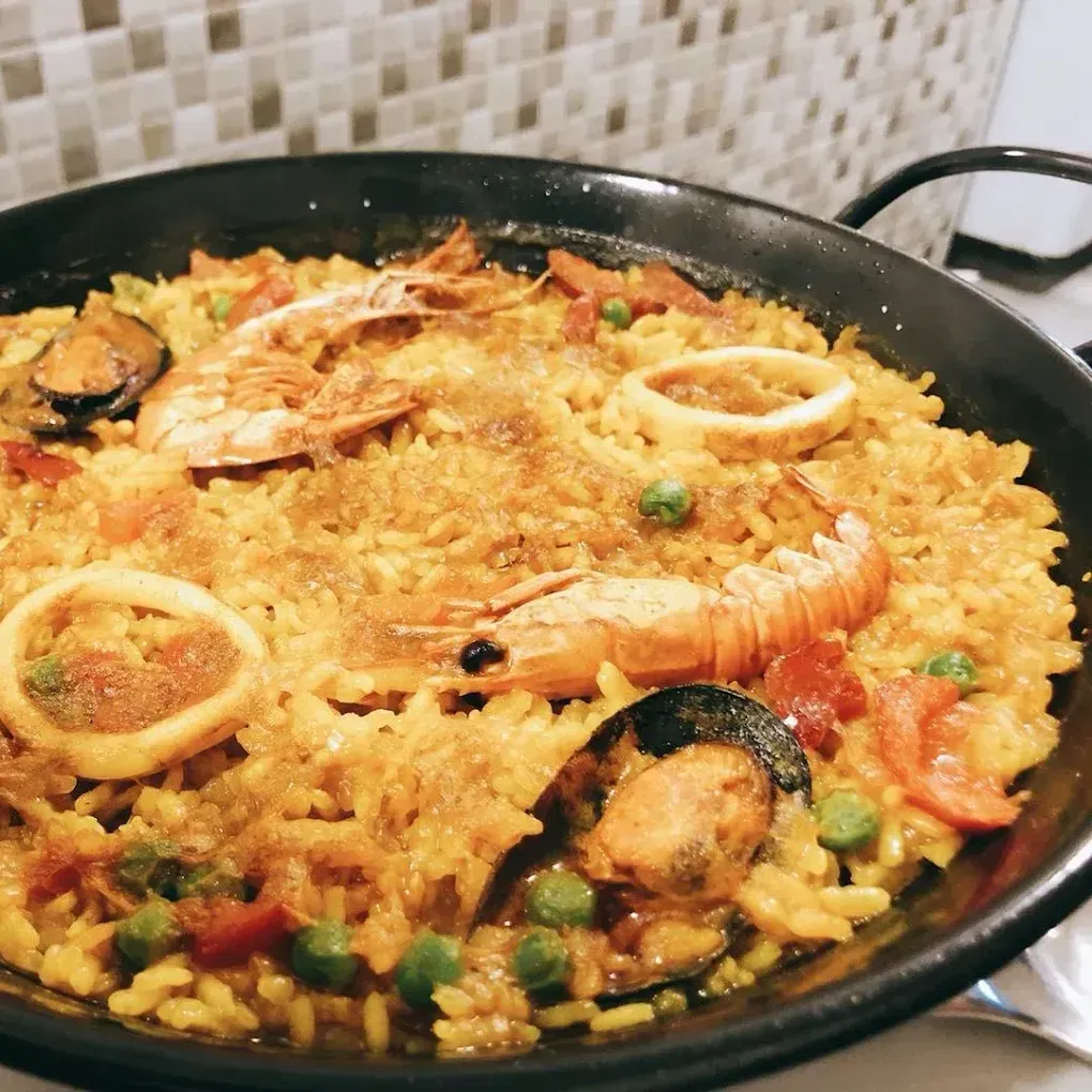 Paella con camarones, mejillones y calamares en sartén negra, con fondo de azulejos.