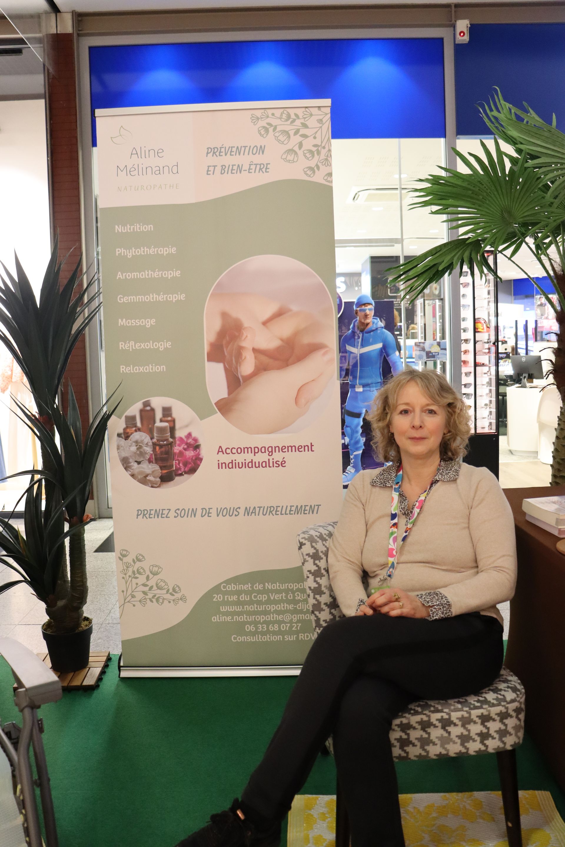 Une femme est assise près d'une banderole publicitaire illustrée, en intérieur.