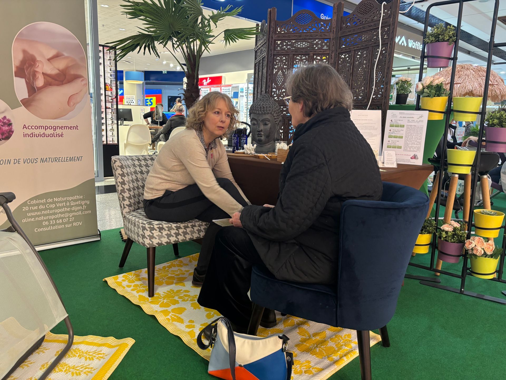 Une femme tient les mains d'une autre personne. Cabine avec plantes, meubles et panneau.