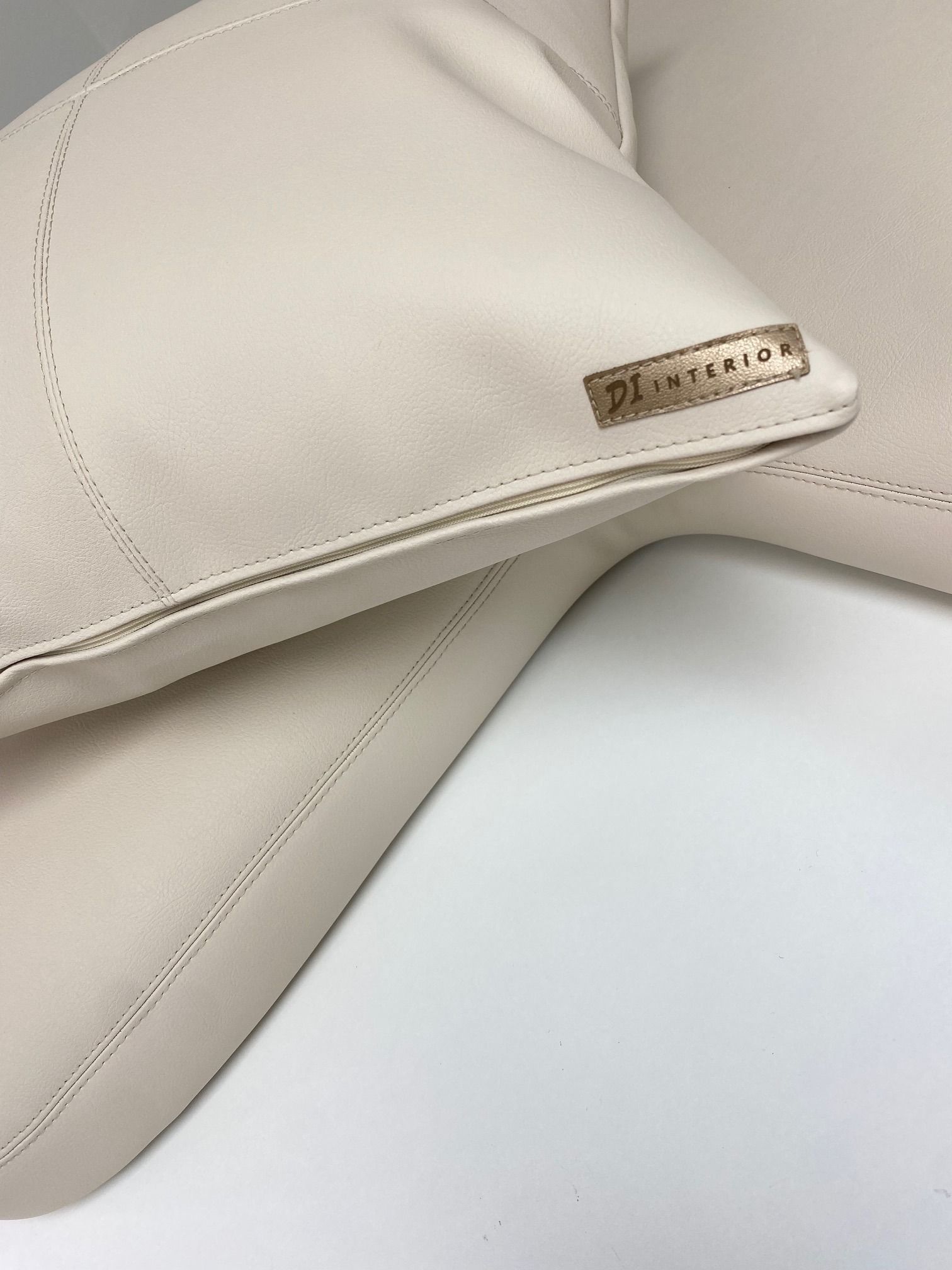 Beige lippalakki, jossa pieni kultainen logo valkoisella taustalla