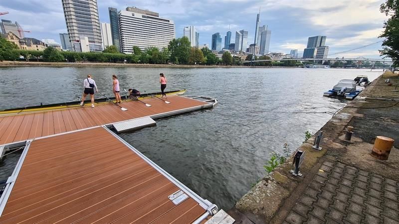 Eine Gruppe von Menschen steht auf einem Steg und blickt auf ein Gewässer.