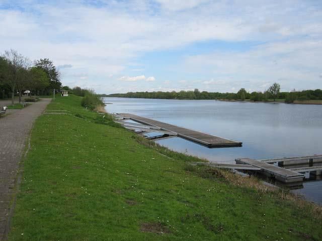 Ein großes Gewässer, umgeben von Gras und Bäumen