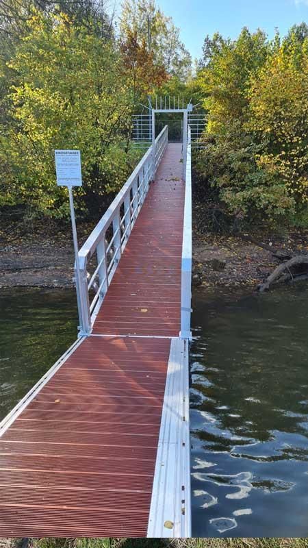 Ein Holzsteg, der zu einem von Bäumen umgebenen Gewässer führt.