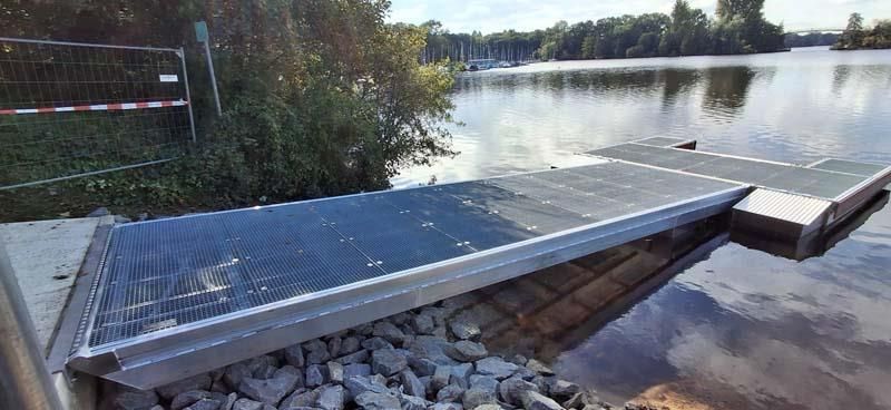 Neben einem Gewässer befindet sich ein Metallsteg.