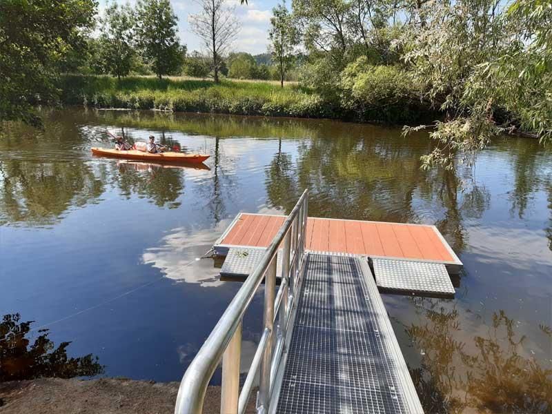 Eine Person fährt in einem Kajak einen Fluss neben einem Dock hinunter.
