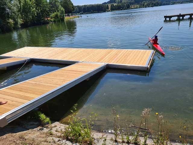 Eine Person paddelt in einem roten Kajak auf einem Holzsteg.