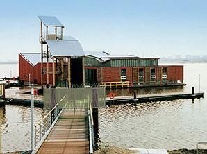 Ein schwimmendes Haus liegt auf einer Wasserfläche neben einem Dock.