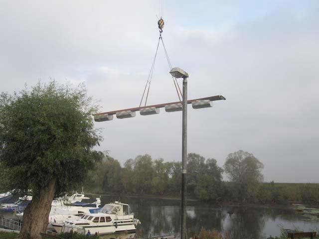 Ein Kran hebt einen Mast über ein Gewässer