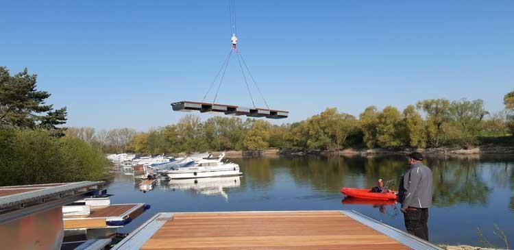Ein Mann steht auf einem Steg neben einem See, während ein Kran ein Boot anhebt.