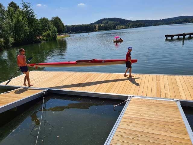 Ein Mann trägt ein rotes Kajak auf einem Holzsteg.