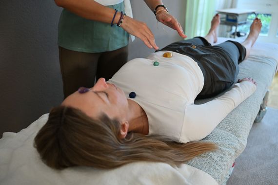 Hände, die während einer Massage heisse Steine ​​auf einen Fuss legen.