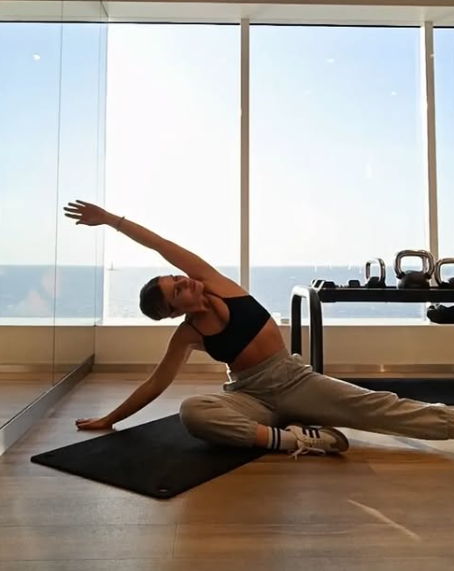 Una mujer está sentada en una esterilla de yoga estirando los brazos.