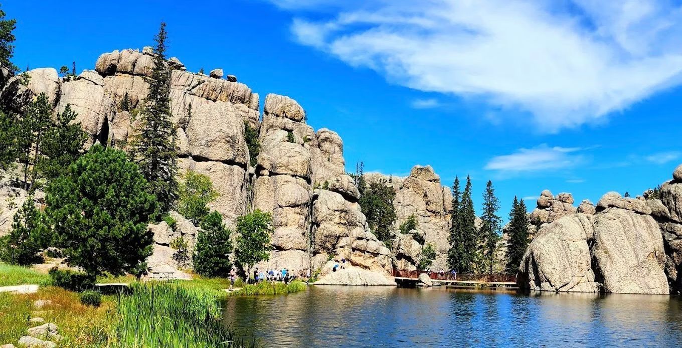 Rocky lakeside cliffs with pine trees under a bright blue sky.