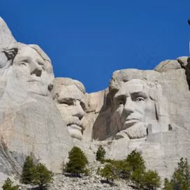 Mount Rushmore carvings against a clear blue sky, with trees at the base