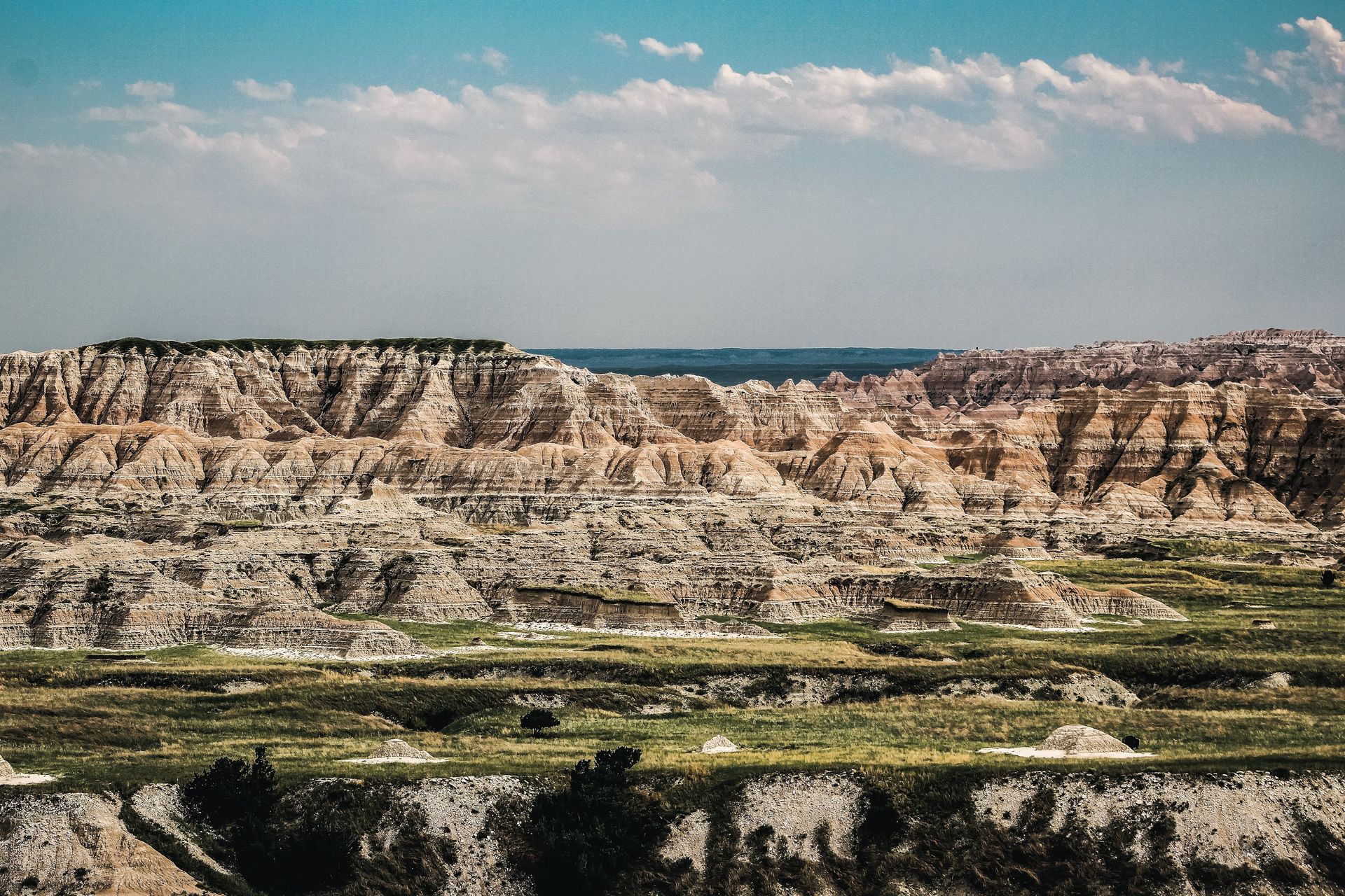 Layered desert cliffs beneath a partly cloudy sky, with green valley vegetation in the foreground