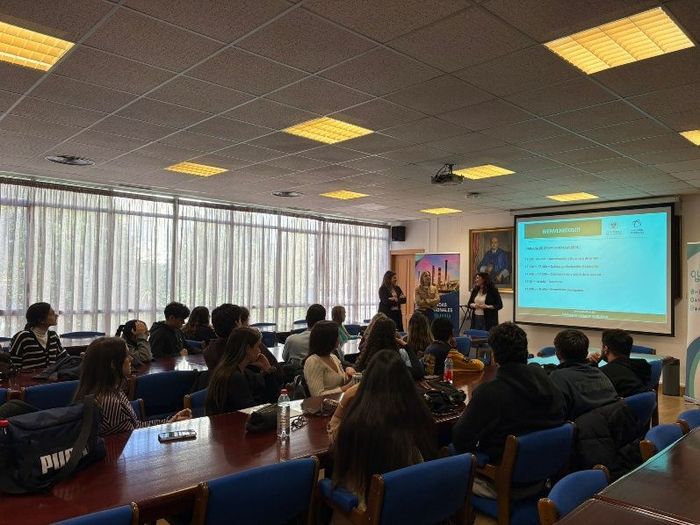 Público sentado en un aula viendo una presentación en una pantalla de proyección.