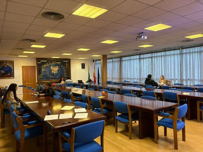 Sillas azules y mesas largas en un luminoso comedor con gente sentada cerca de las ventanas.