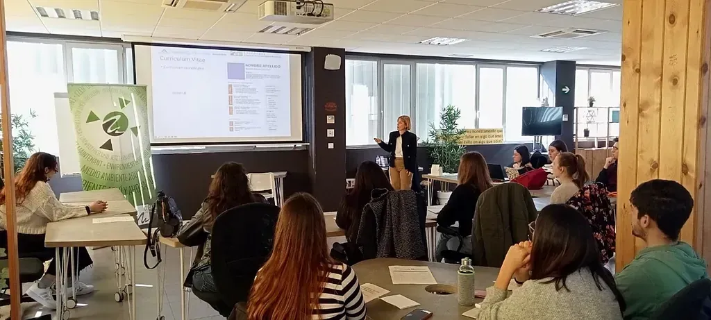 Un presentador habla con un grupo de estudiantes en un aula con una presentación en una pantalla.