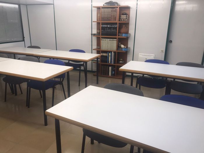 Un aula con mesas blancas y sillas azules.