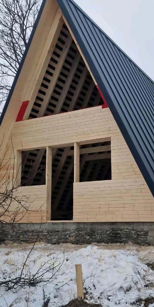 Cabaña en construcción con techo de metal negro y paredes de madera sin terminar, en un paisaje nevado.