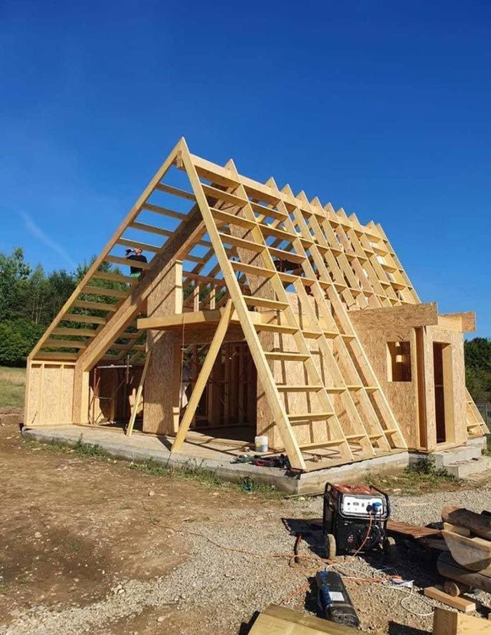 Casa de madera con estructura en forma de A en construcción en un día claro, con cielo azul.