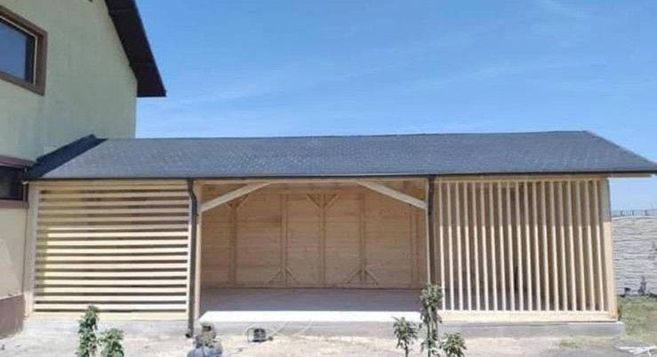 Estructura de madera con techo oscuro, adosada a un edificio. Presenta paredes de listones y un interior arqueado.