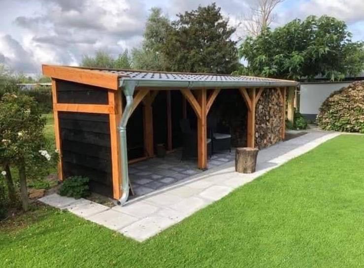 Refugio exterior de madera con leña, césped verde y un patio de baldosas grises.