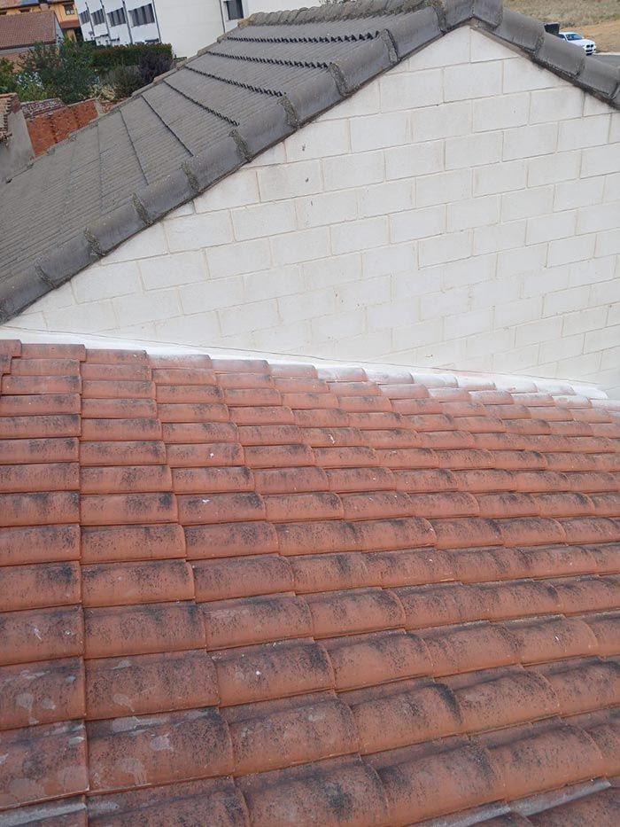 Techo de tejas rojas se encuentra con pared blanca y techo gris.