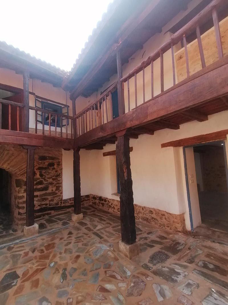 Patio con suelo de piedra, paredes blancas y balcón de madera. Columnas y molduras marrones.