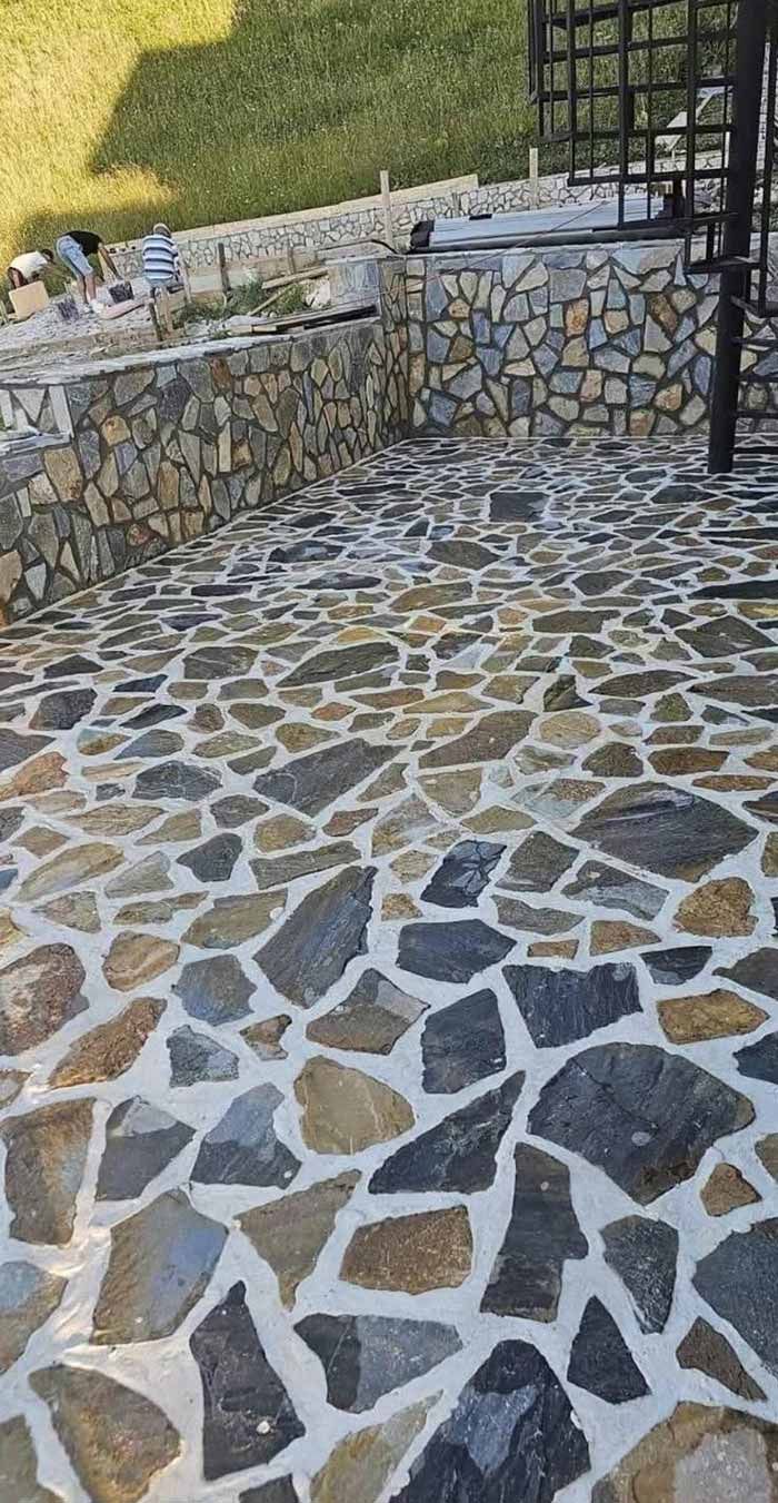 Patio de piedra con patrón de mosaico decorativo; muro de piedra adyacente y césped.