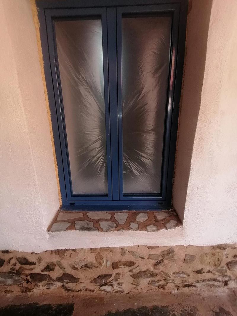 Ventana con marco azul y vidrio esmerilado situada en una pared blanca sobre una base de piedra.