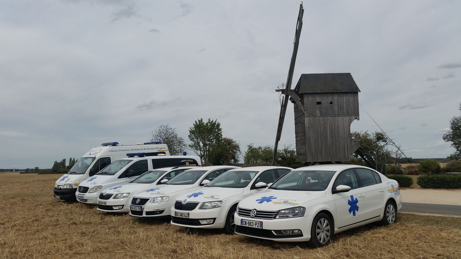 Des ambulances blanches garées dans un champ à côté d'un petit moulin à vent 