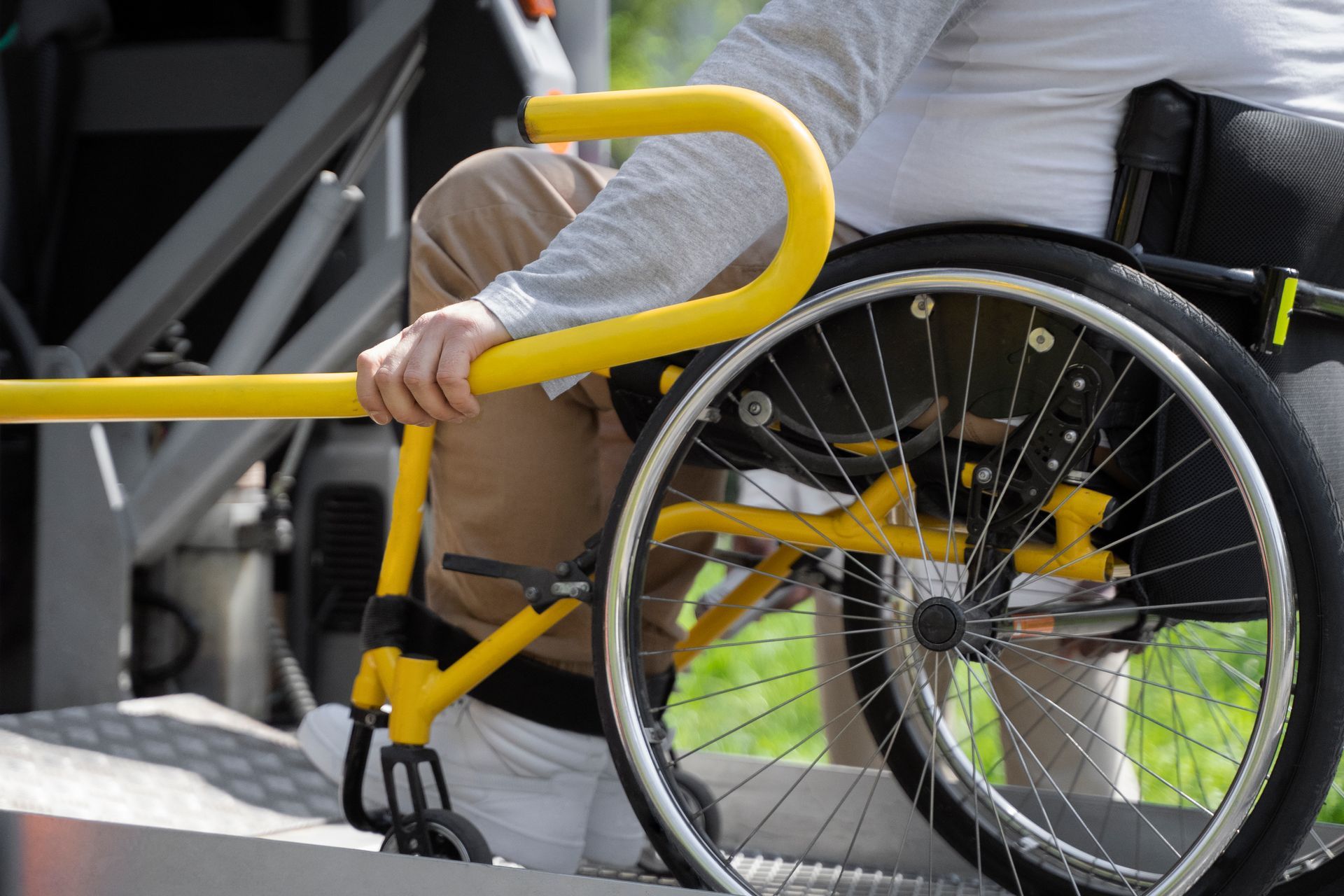 Personne en fauteuil roulant utilisant une main courante jaune sur une rampe.