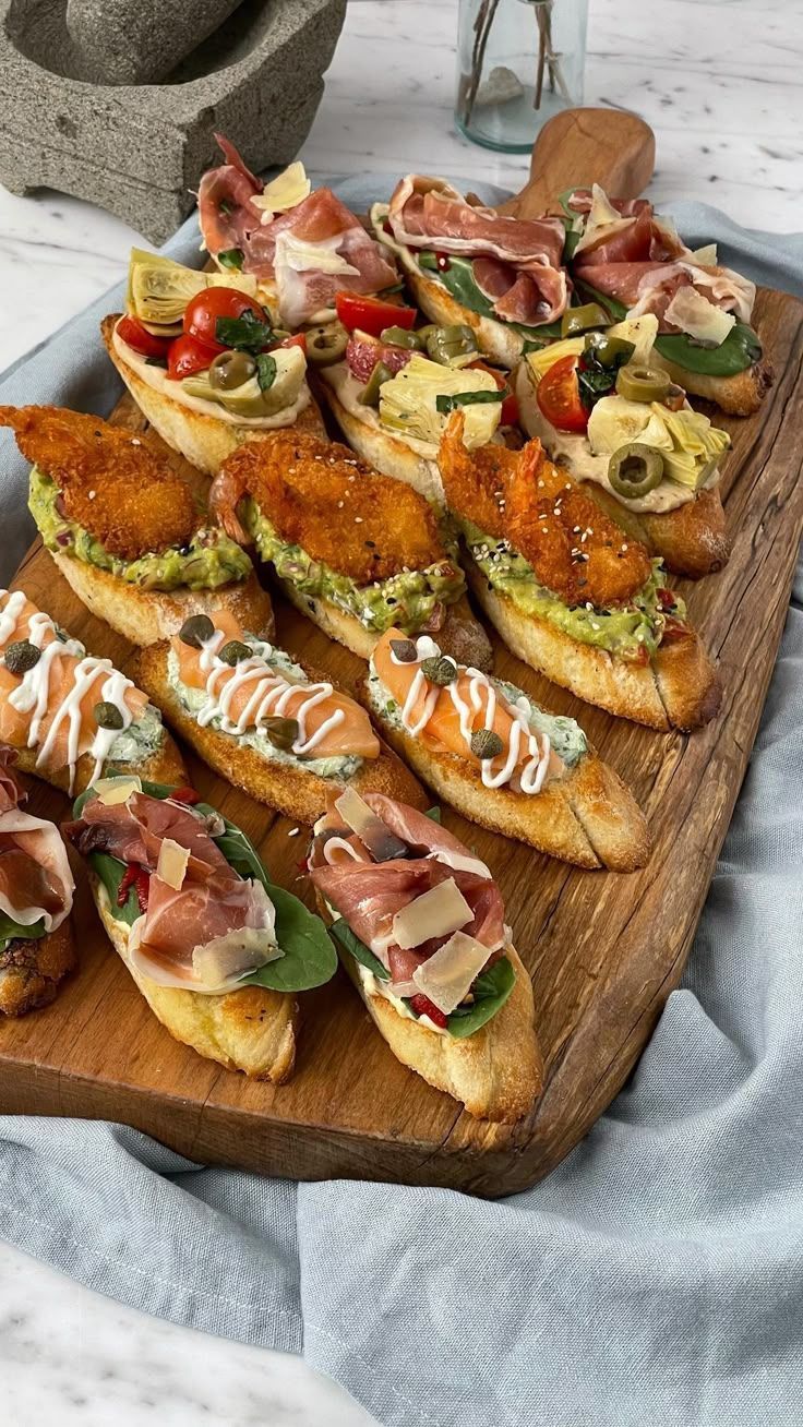 Tabla de madera con bruschetta variada: pollo frito, prosciutto, verduras, aceitunas.