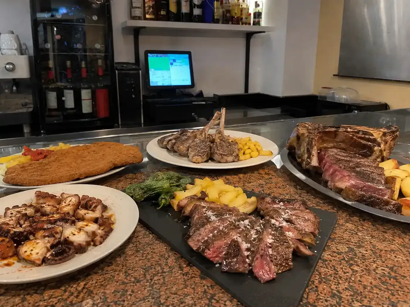 Variedad de carnes a la parrilla y guarniciones en platos sobre una encimera en una cocina o comedor.