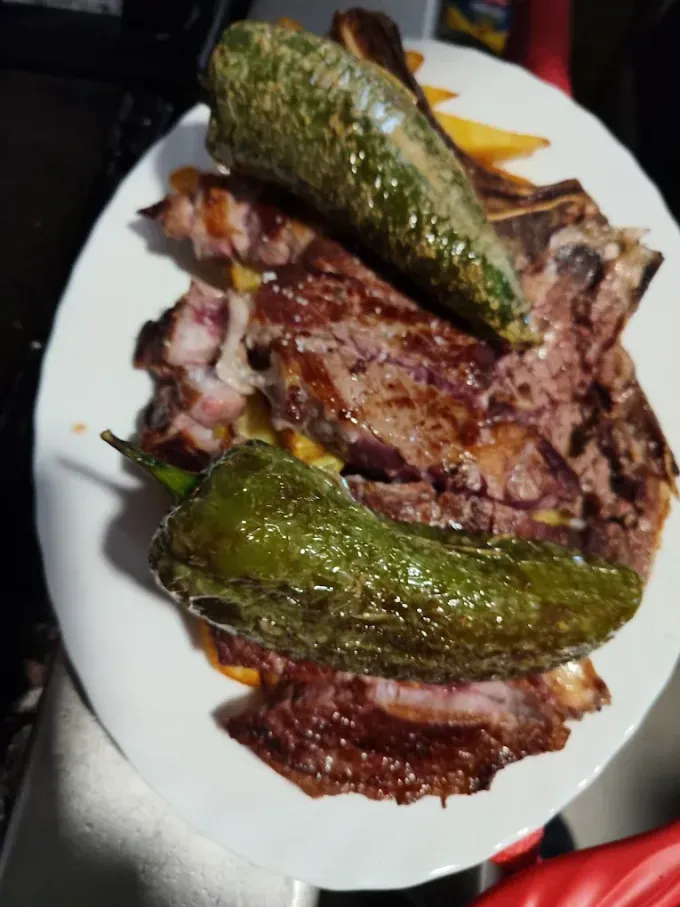 Filete a la parrilla cubierto con dos pimientos verdes asados en un plato blanco.