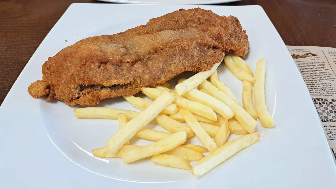 Chuleta de carne empanizada con patatas fritas en un plato blanco.