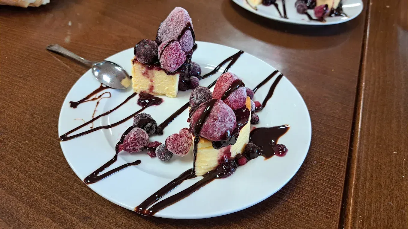 Postre en plato blanco: cuadrados de pastel con frutos rojos confitados y un toque de chocolate. Mesa marrón, cuchara.