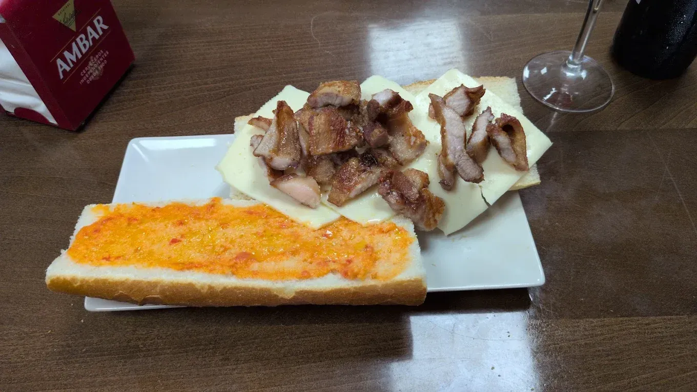 Sándwich abierto con carne y queso en un plato blanco, junto a tostadas