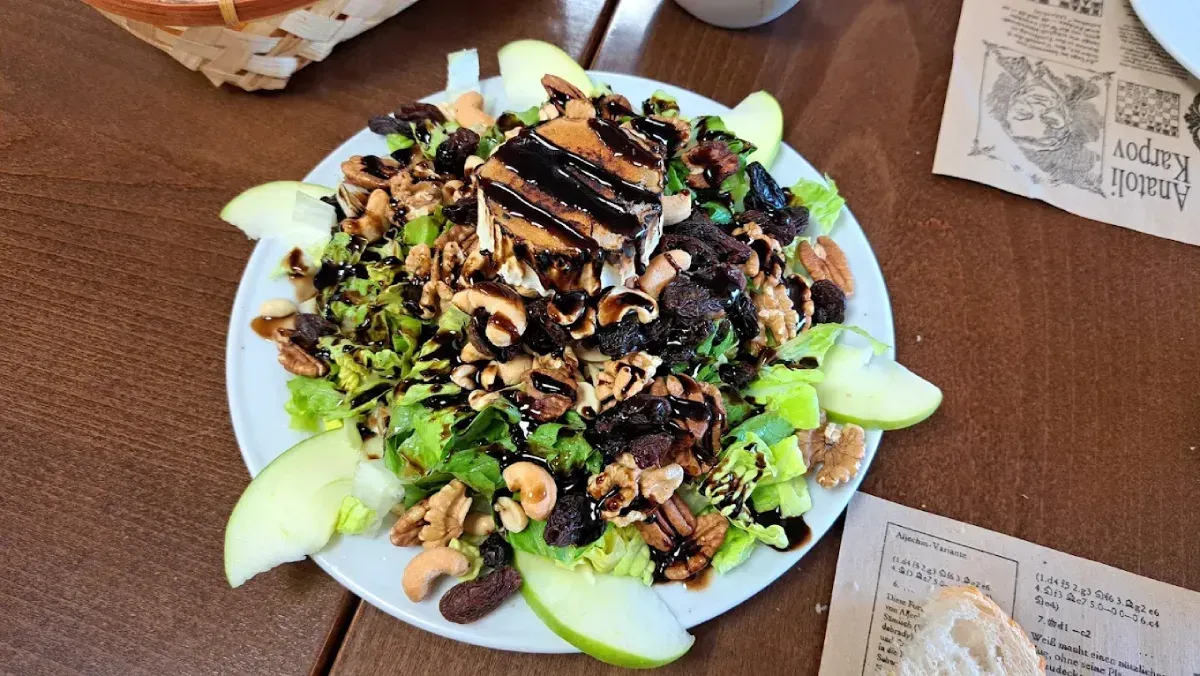 Ensalada con verduras, nueces, rodajas de manzana y glaseado balsámico en un plato blanco, mesa de madera.