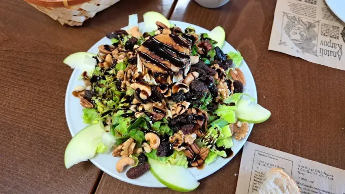 Ensalada con verduras, nueces, rodajas de manzana y glaseado balsámico en un plato blanco, mesa de madera.