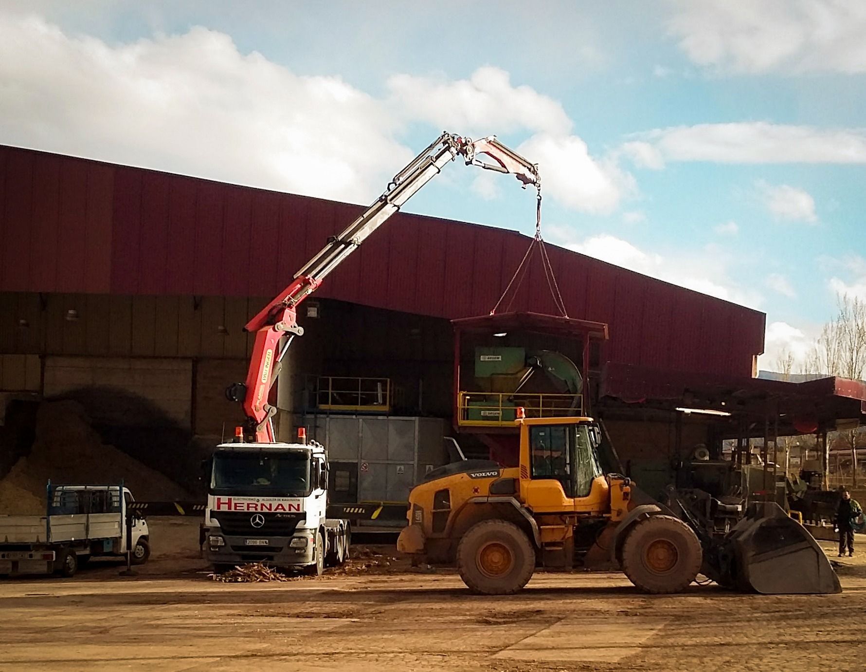 Vehículos de construcción cargando escombros en un sitio industrial bajo un cielo nublado.