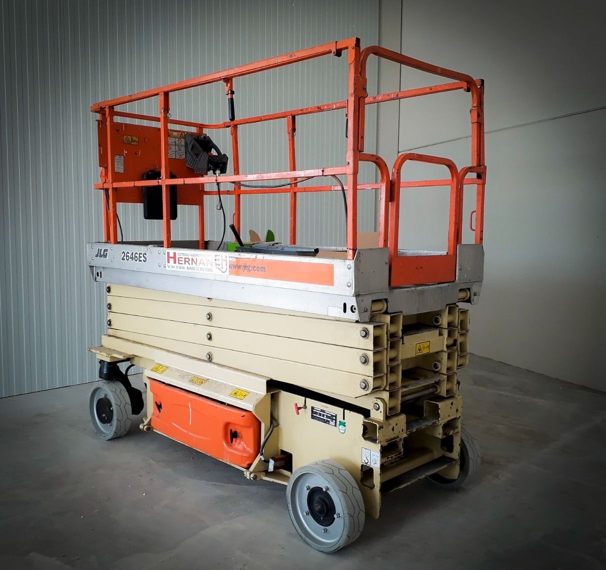 Plataforma elevadora de tijera naranja con barandillas elevadas en un entorno de almacén interior.