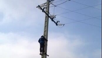 Un trabajador de servicios públicos trepa a un poste de luz bajo un cielo nublado.